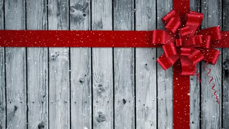 Video-composition-with-snow-over-Christmas-gift--ribbon-on-wood