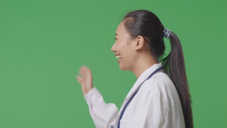 close up of side view asian female doctor with stethoscope waving hand and smiling while walking on green screen background in the hospital