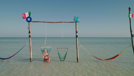 turista femenina con sombrero de paja en bikini columpiándose en una silla, hamacas holbox