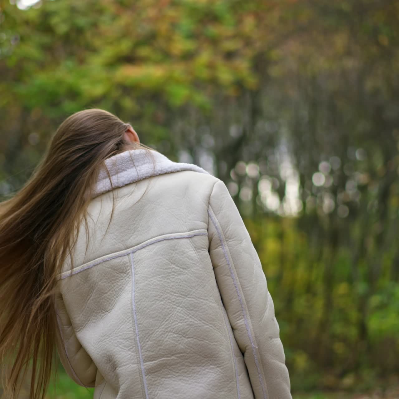 Caucasian lady walking in the nature turns around waving her beautiful long hair. Blurred natural autumn backdrop