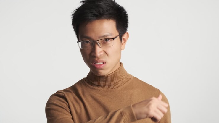 Asian man in eyeglasses showing threatening gesture.