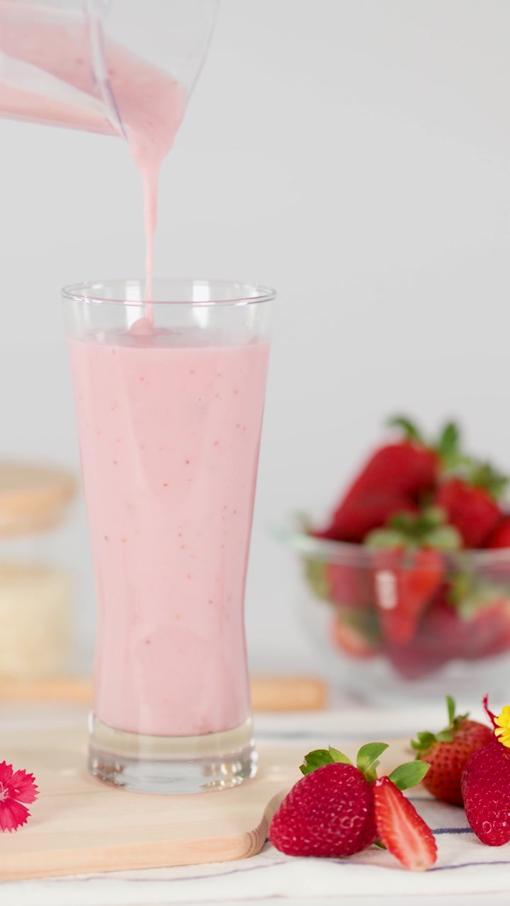 Frullato cremoso rosa alla fragola versato in un bicchiere, circondato da fragole fresche, fiori, illuminazione brillante
