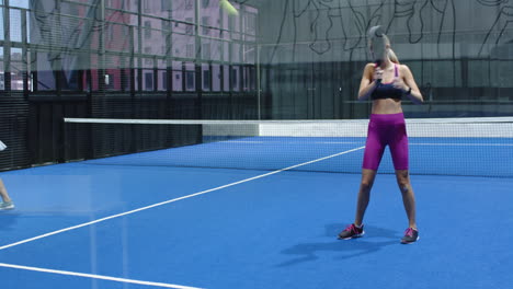 woman playing padel tennis on blue indoor court, focusing on hitting ball