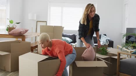 Happy diverse female couple talking and holding boxes during moving home