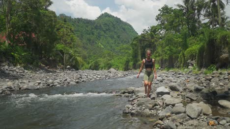 Woman-walking-along-rocky-river-stopping-to-clean-herself-with-fresh-water