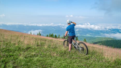 Macho-Adulto-En-La-Cima-De-La-Colina-De-Hierba-Cabalgando-En-Bicicleta-Eléctrica,-Kope,-Eslovenia