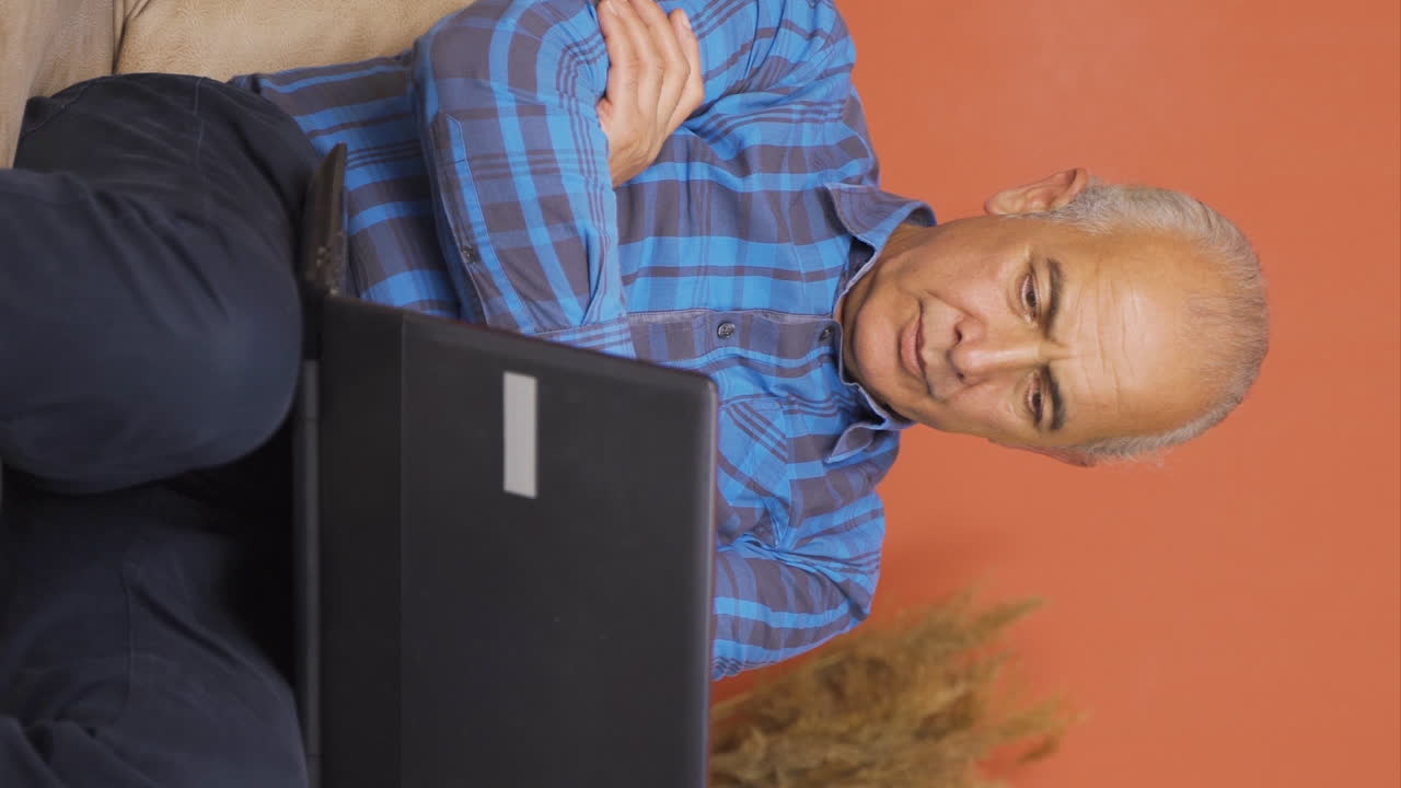 video vertical de un anciano viendo una película en una computadora portátil con una expresión feliz.
