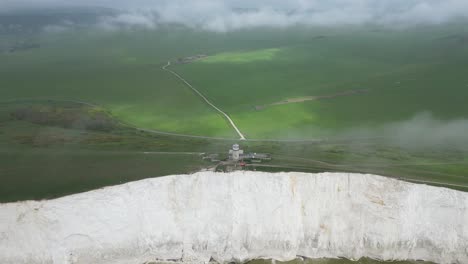 Flying-around-Belle-Tout-Lighthouse,-white-cliffs,-foggy-sky-and-sea