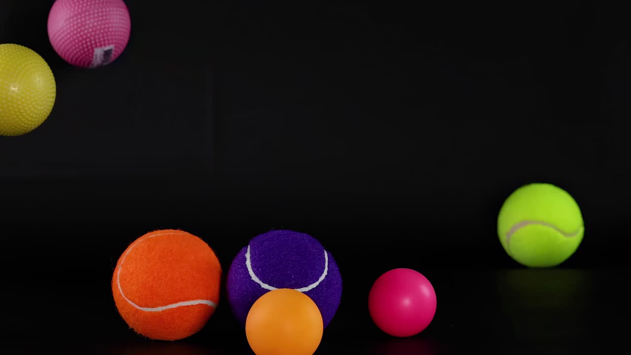 Des balles colorées de différentes tailles rebondissent énergiquement sur une surface sombre, mettant en valeur un mouvement dynamique et des teintes vives.
