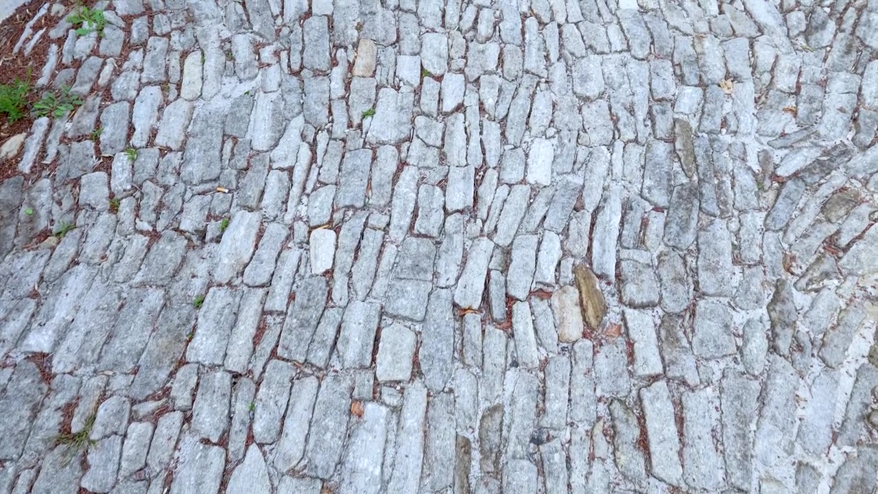 Una telecamera si muove lentamente su un rustico selciato di ciottoli grigi in un villaggio storico francese.