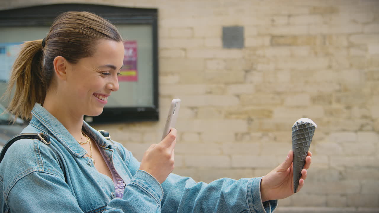 mujer joven tomando una foto de un cono de helado con un teléfono móvil para publicarlo en las redes sociales