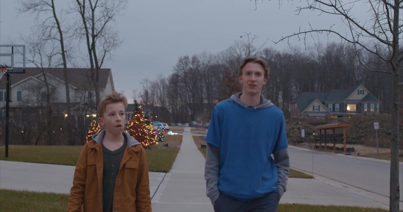 two boys walk toward the camera down the sidewalk