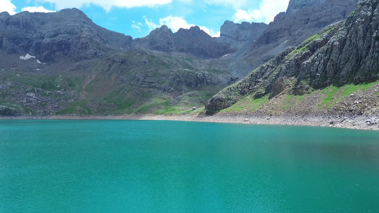 Aerial zoom in over peaceful emerald lake nestled between sharp rock formations in Valle de Ip., Aragon, Spain