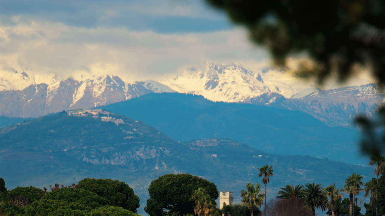 Distant view of orange villas surrounded by green trees with the mountains on the background on a cloudy day