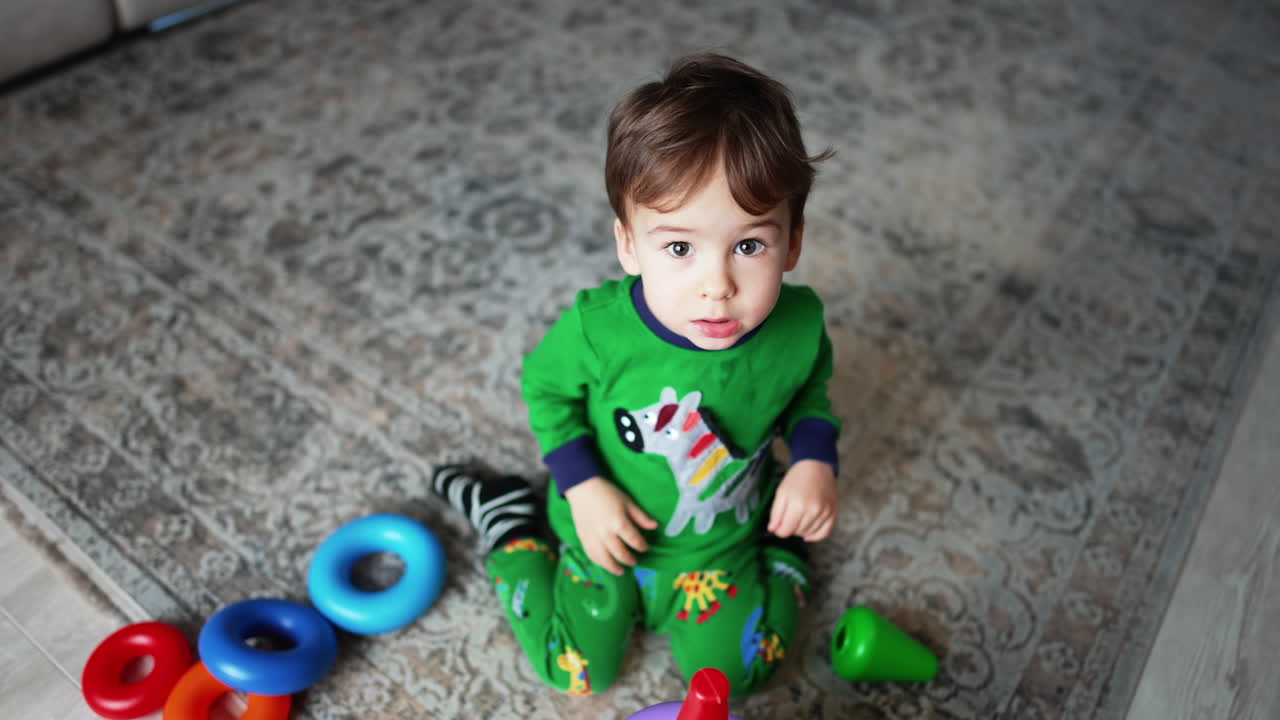 Lovely Caucasian baby boy sits on the floor. Adorable kid assembling a toy pyramid. Top view.