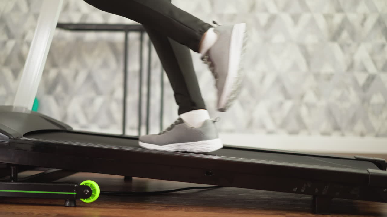 Athlete strolls on treadmill in household closeup. Athletic woman has legs training on workout equipment in personal fitness studio. Active life