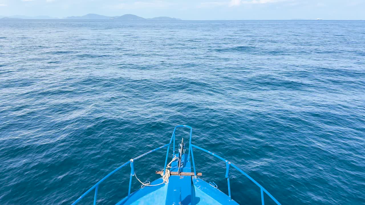 A boat glides smoothly over calm ocean waters near Phuket, Thailand, under clear skies with distant islands visible