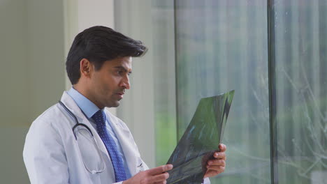 male doctor wearing white coat standing in hospital corridor looking at ct or mri scan