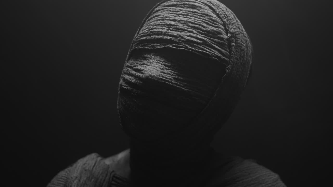 A mummy of a woman on a dark backdrop slowly rises her head