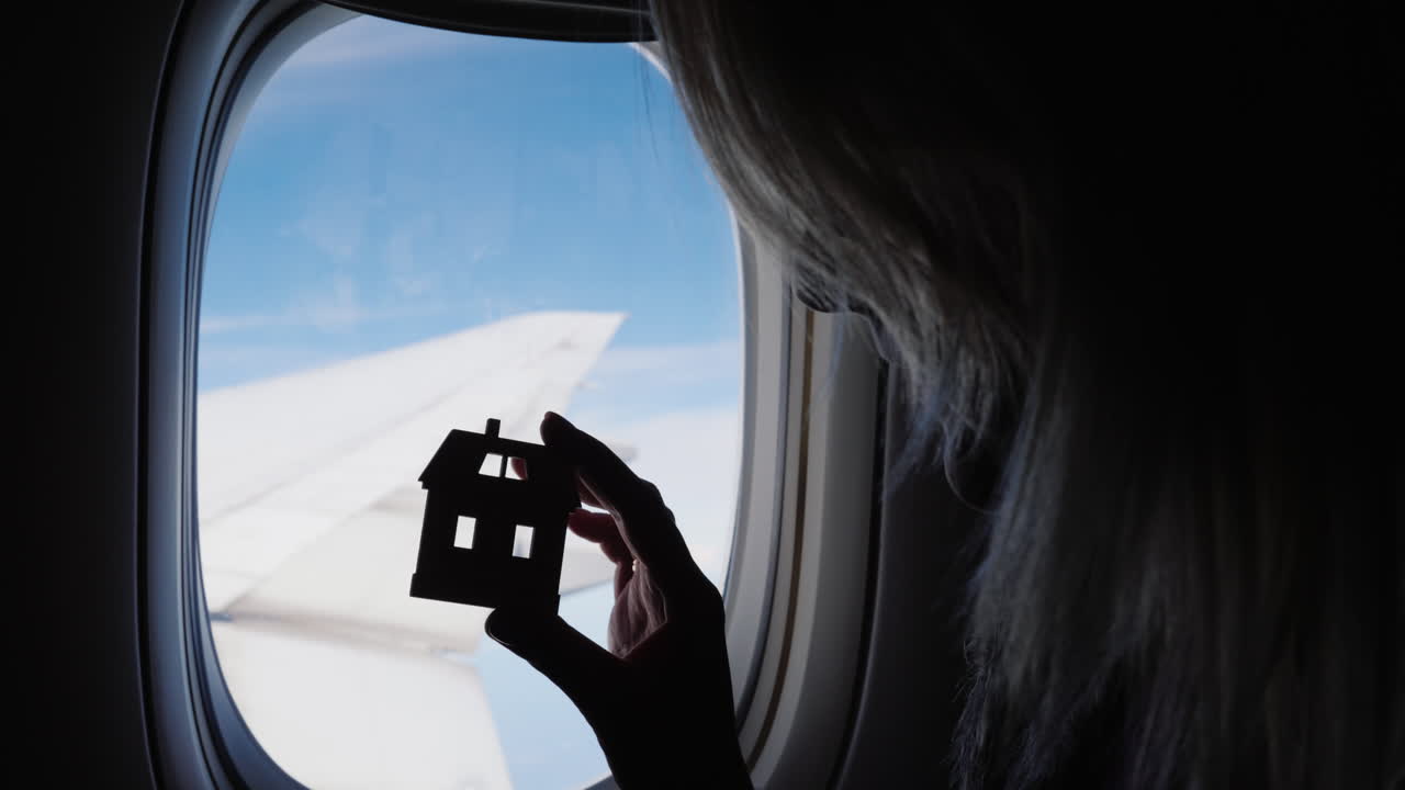 mujer sosteniendo una figurilla de la casa junto a la ventana del avión