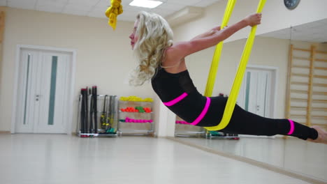 the girl is engaged in aero yoga in a white studio flying over the floor on the canvases in slow motion. relaxation and relaxation through stretching