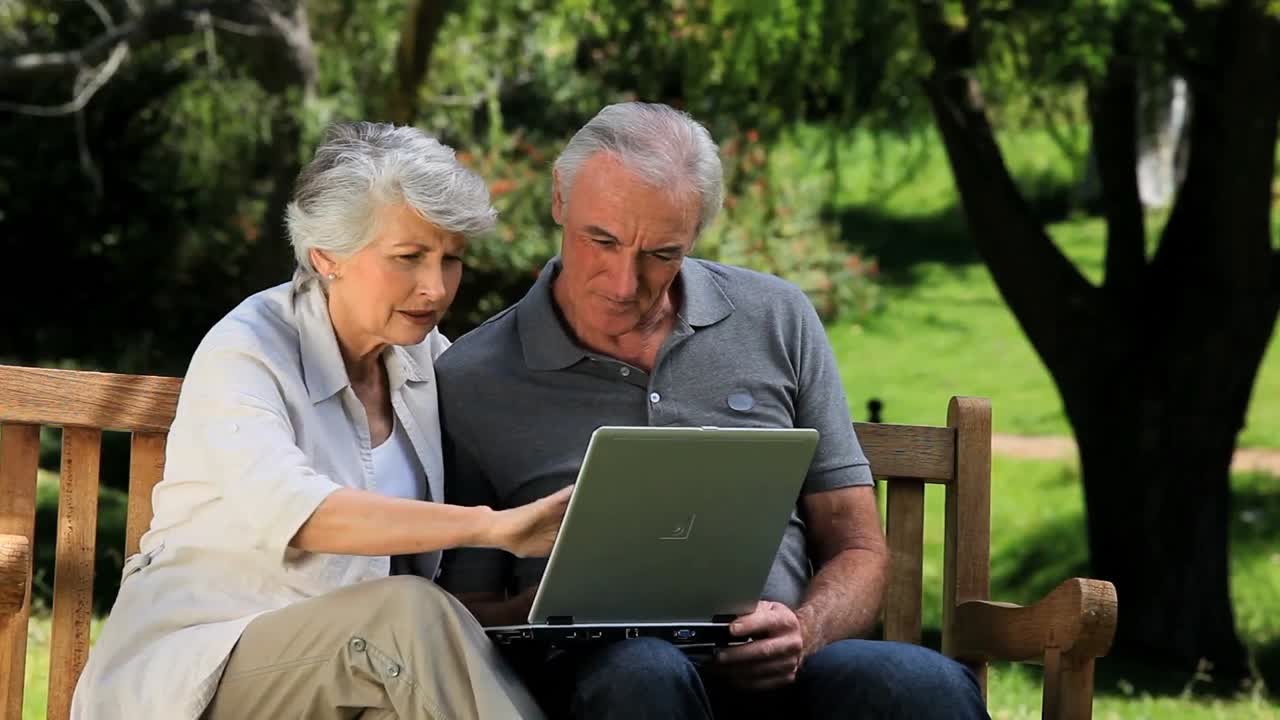 uomo e donna anziani che guardano un laptop seduti su una panchina