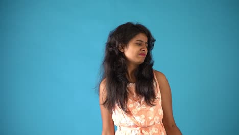 a young indian girl in orange frock trying hard to lift dumbbells standing in an isolated blue background
