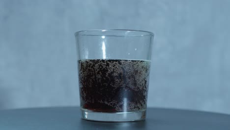 in a slow-motion pour, a small glass of root beer soda rotates right to left