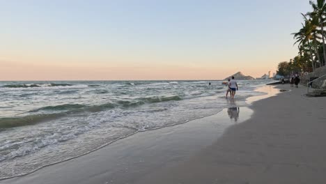 two people and a dog walking on the beach at sunset