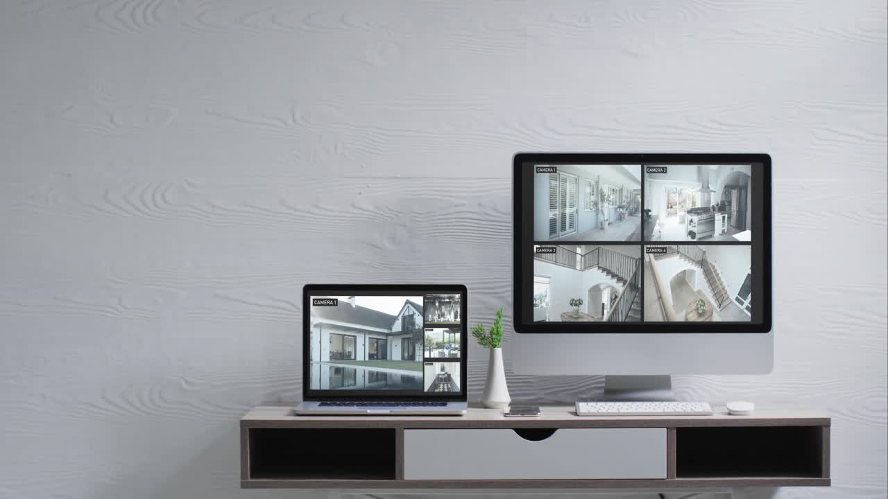 Wall mounted computer monitor and laptop on desk with security camera views on screens, slow motion