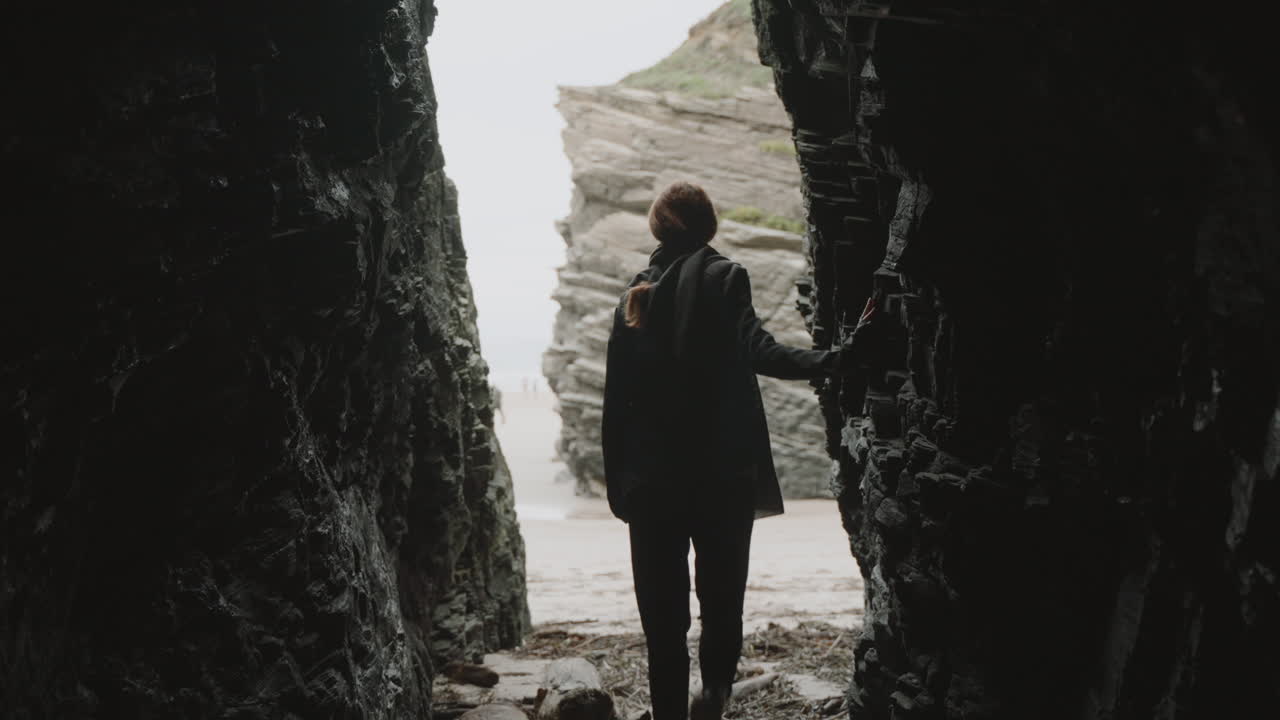 Person Exiting a Dark Cave onto a Bright Coastal Beach