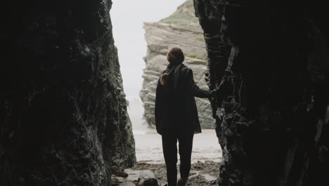 person exiting a dark cave onto a bright coastal beach