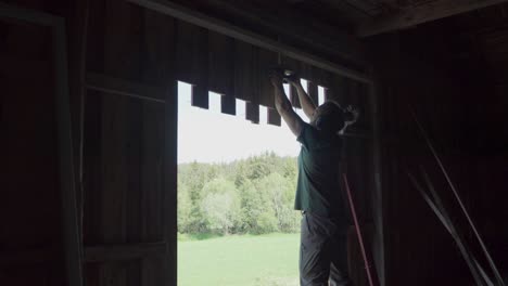Carpenter Cutting Wooden Plank Wall Of A Barn House Using Electric Saw