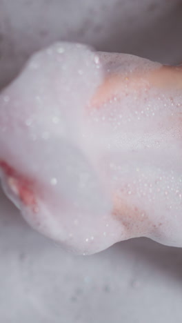 woman plays with fluffy foam in bathtub closeup. lady holds handful of soap bubbles resting in cozy bathroom. woman relaxes during hygienic routin