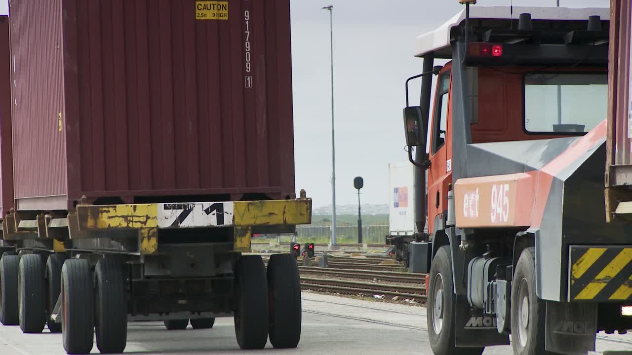 Trucks transport containers at Rotterdam port, showcasing industrial activity