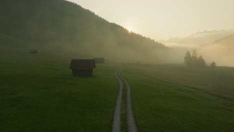 Misty-morning-over-grassy-fields-and-farm-huts-at-Wagenbrüchsee-in-Germany,-aerial-view