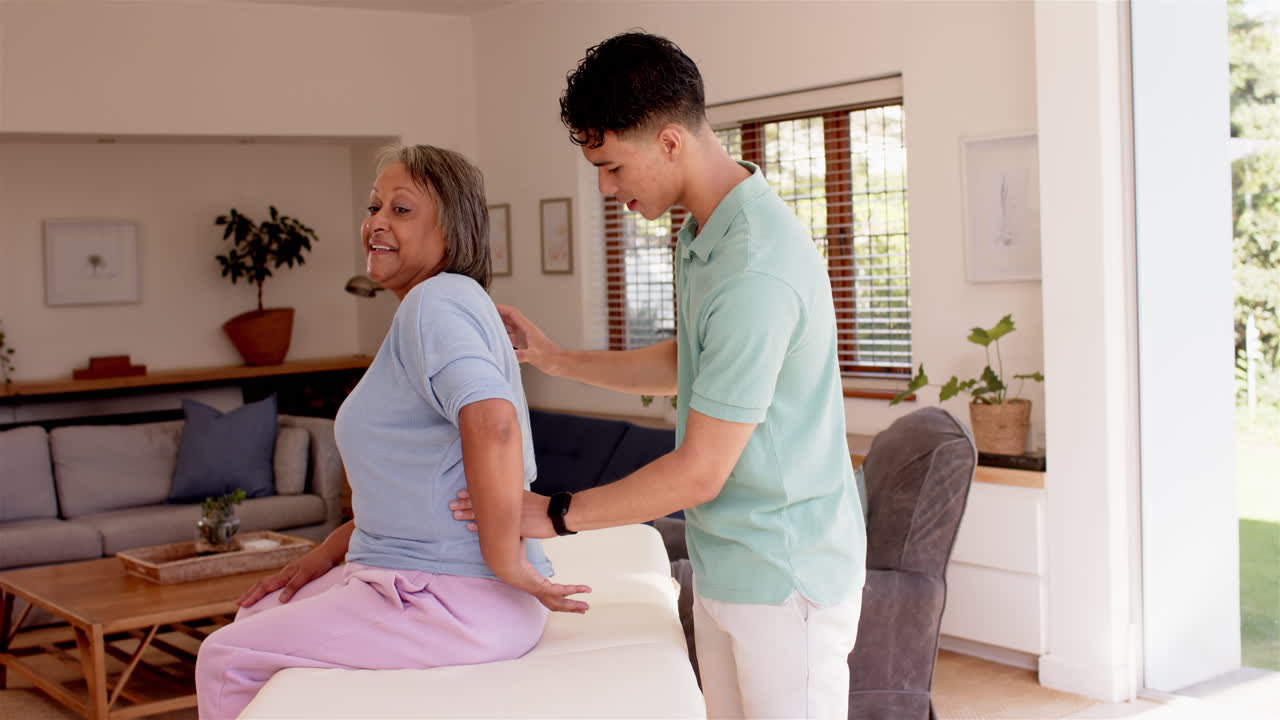 Assisting senior woman, male physiotherapist performing back therapy in living room