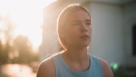 close up of young lady looking thoughtful, sunlight illuminating her face with a warm glow, moving gracefully like roller skating, partial view of building and trees in blurred background