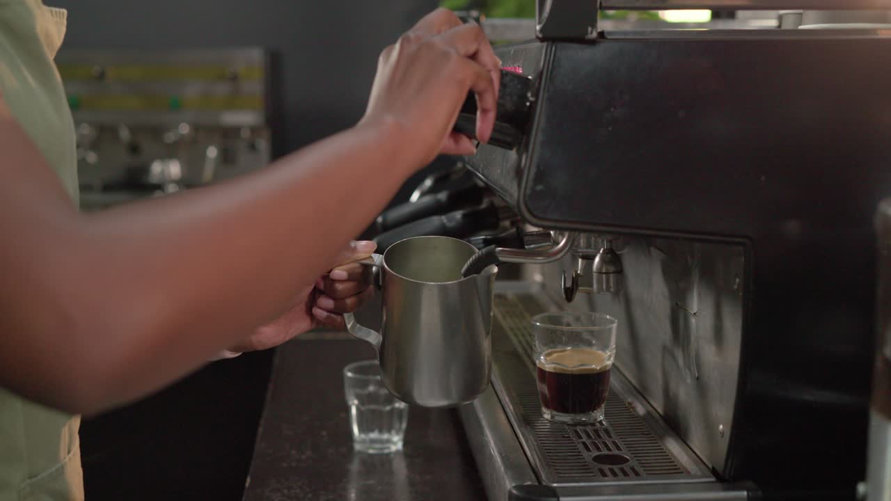 Le mani del barista si allungano verso la manopola di controllo e vaporizzano il latte nel bricco alla macchina da caffè espresso per un latte macchiato.