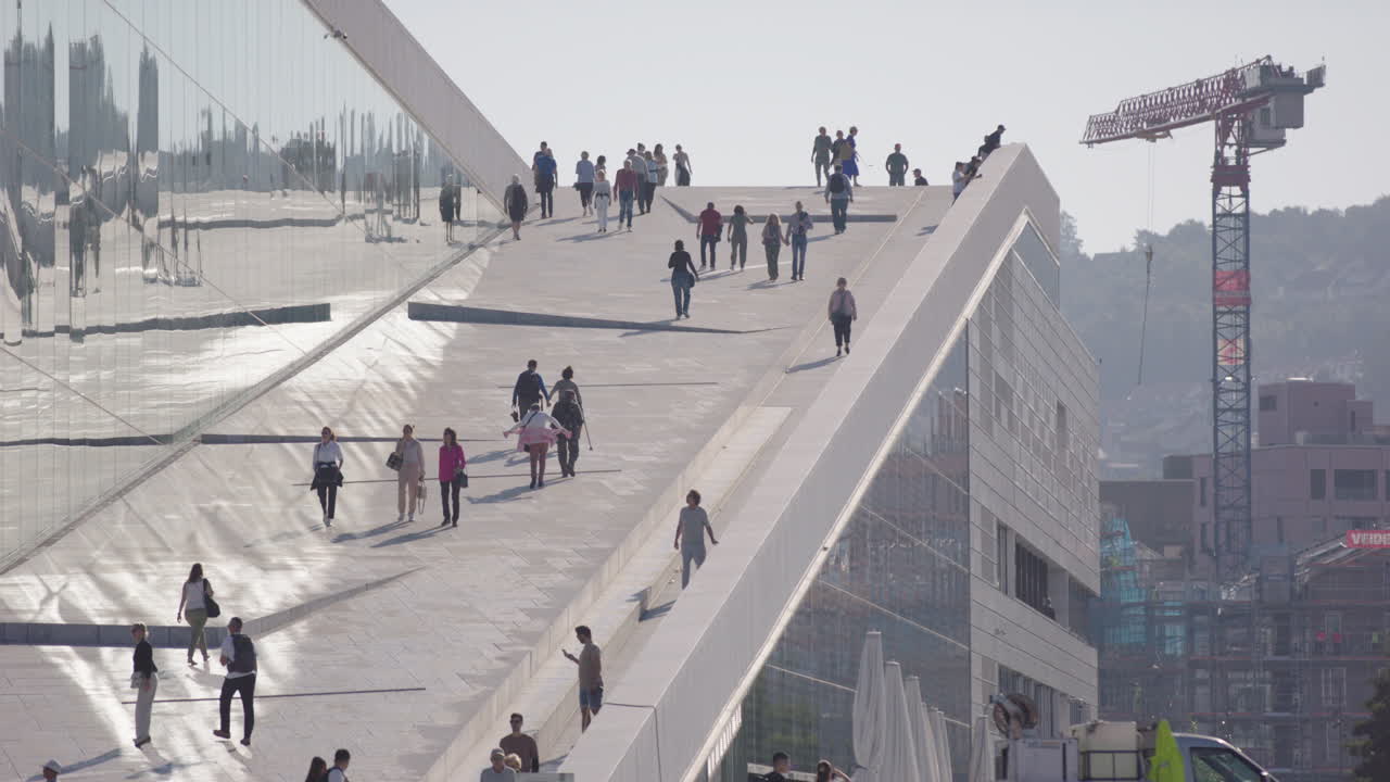 Citizens walk on sloped marble roof of contemporary Oslo Opera House, slomo