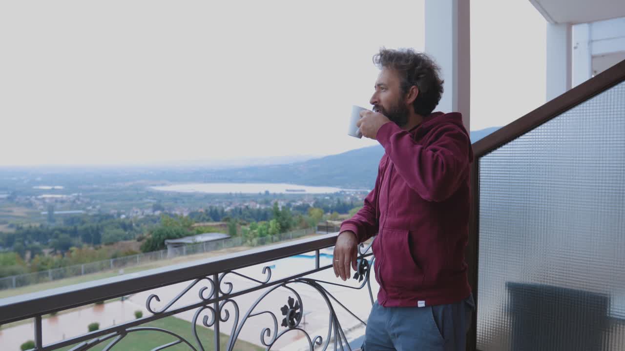 hombre de pie de la silla y mirando hacia el horizonte en un balcón con una vista impresionante mientras sostiene una taza de café