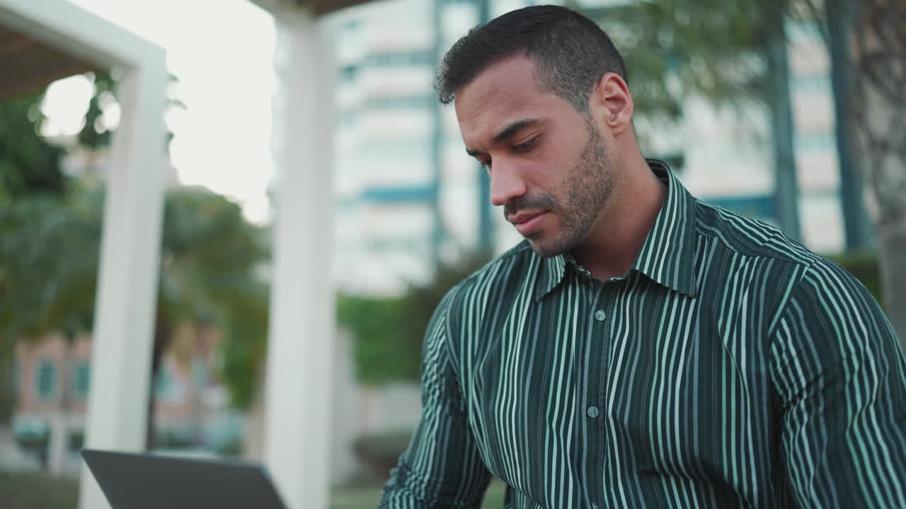 Giovane uomo che usa il laptop seduto su una panchina all'aperto