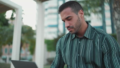 young man using laptop sitting in bench outdoors.