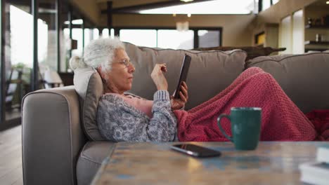 Senior-mixed-race-woman-lying-on-sofa-using-tablet