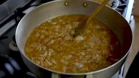 cebollas picadas revueltas en salsa de curry en una olla grande de acero con espátula de madera