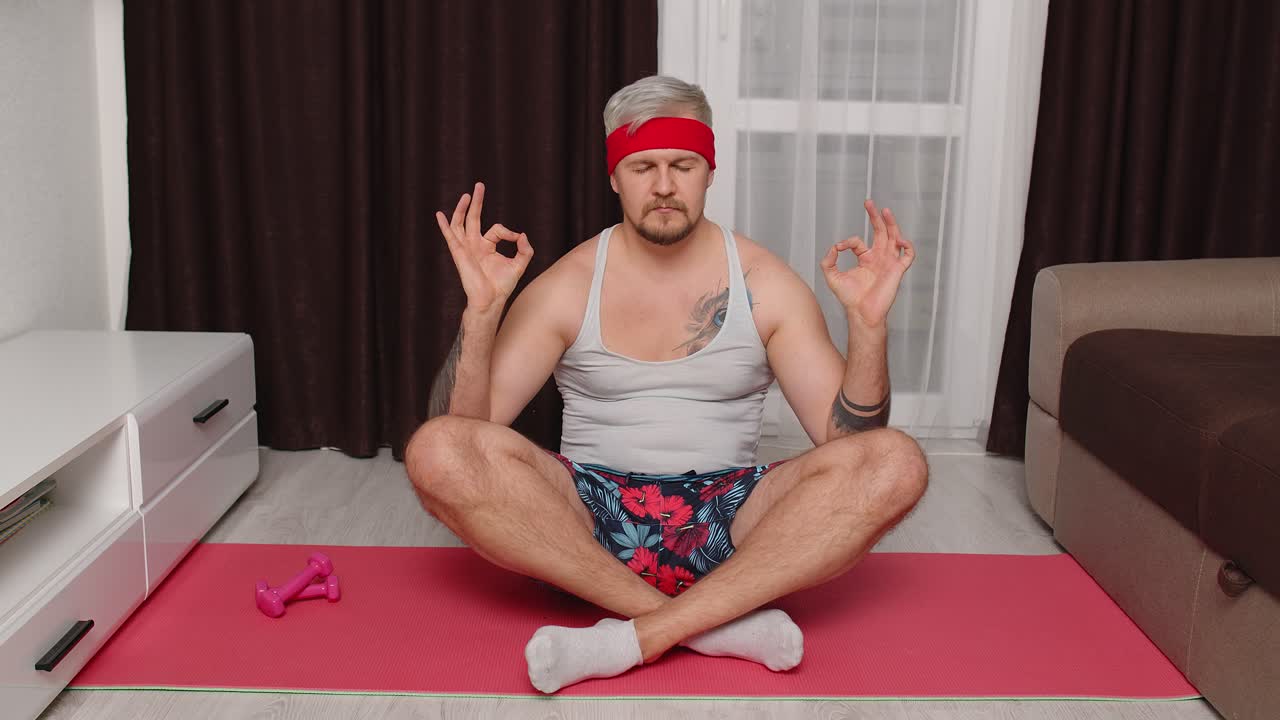 modelo masculino retro se calma, practicando yoga meditando en casa sentado en una relajante postura de loto