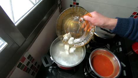 mujer arrojando raviolis en una olla roja con agua hirviendo