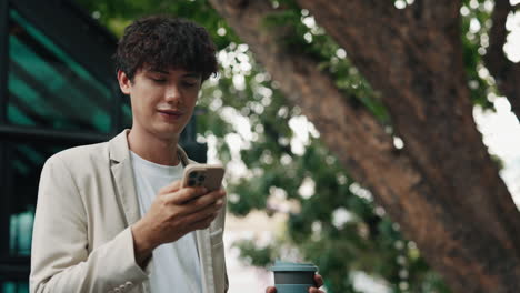 man using smartphone with coffee cup outdoors