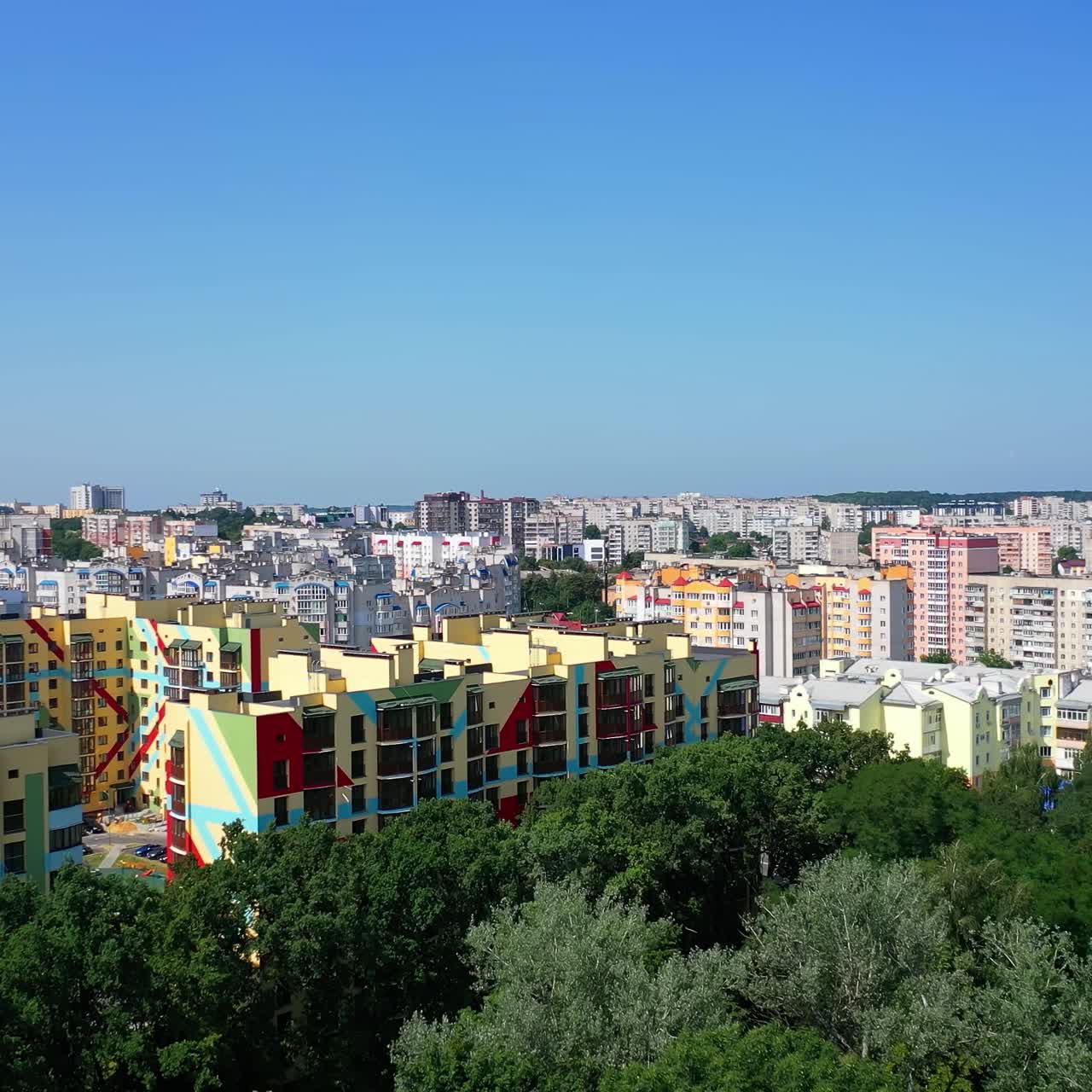 Colorful residential complex in the city. Flight over green trees on the urban background. Contemporary part of a city. Aerial view