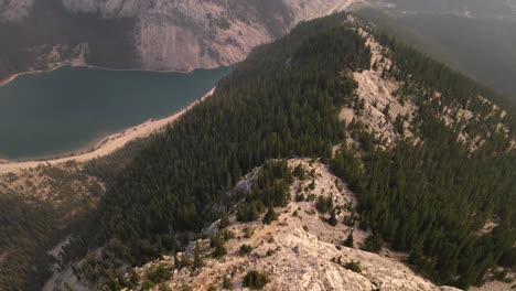 Aerial-4K-footage-of-a-drone-flying-over-a-mountain-with-lot-of-pine-trees-and-big-blue-lake-at-the-base-during-a-wildfire